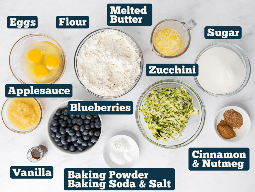 Zucchini blueberry muffin ingredients: Applesauce, Eggs, Flour, Melted Butter, Sugar, Cinnamon and Nutmeg, Zucchini, Salt,Baking Soda, Baking Powder, Blueberries, and Vanilla