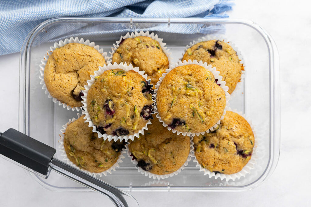 Fully cooled zucchini blueberry muffins in an airtight container for storage.