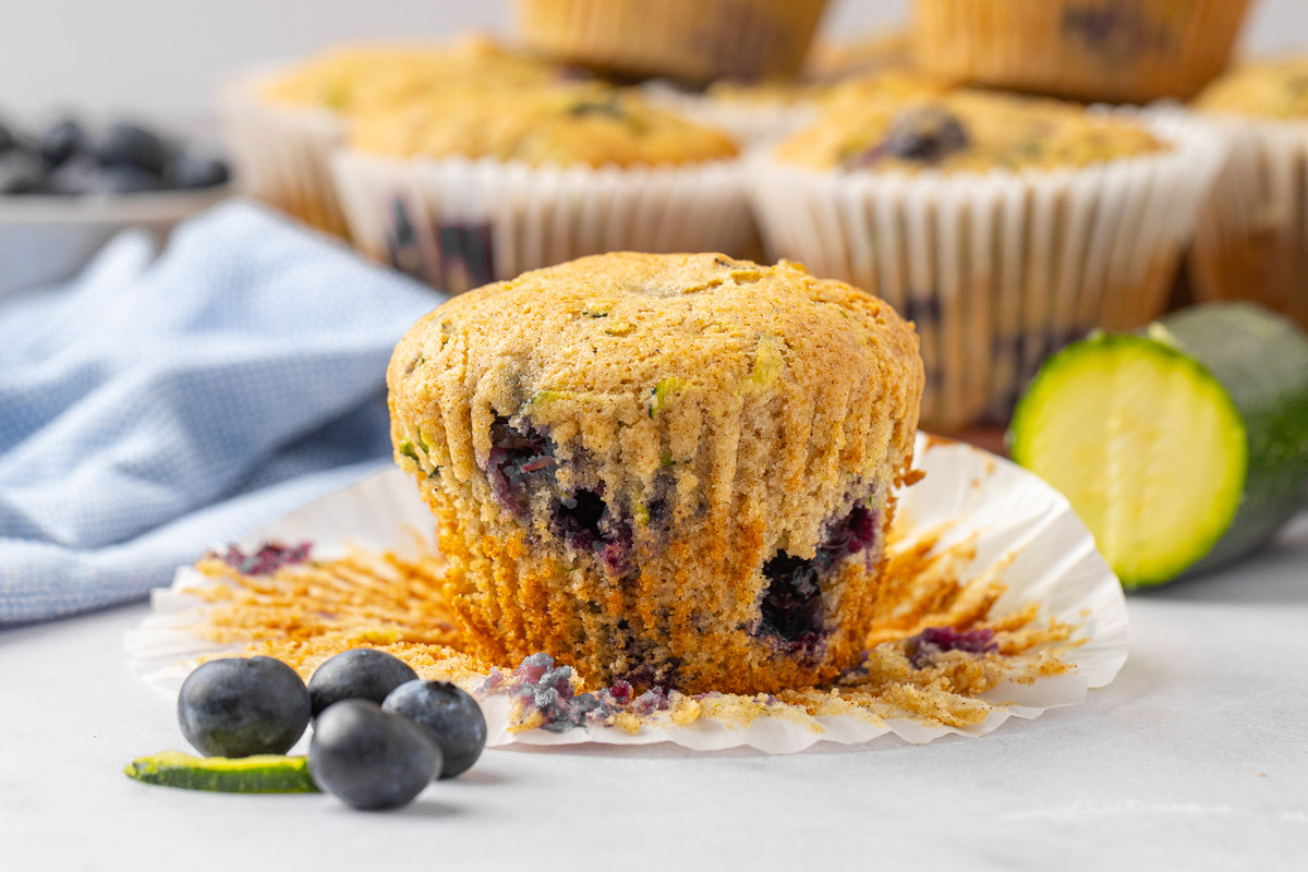 Zucchini blueberry muffin sitting on an opened muffin liner.