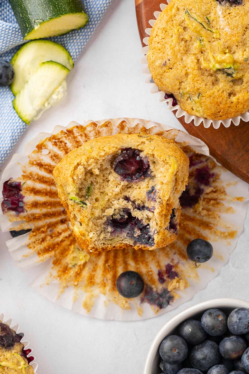 Zucchini blueberry muffin with a bite taken out of it sitting on an open muffin liner.