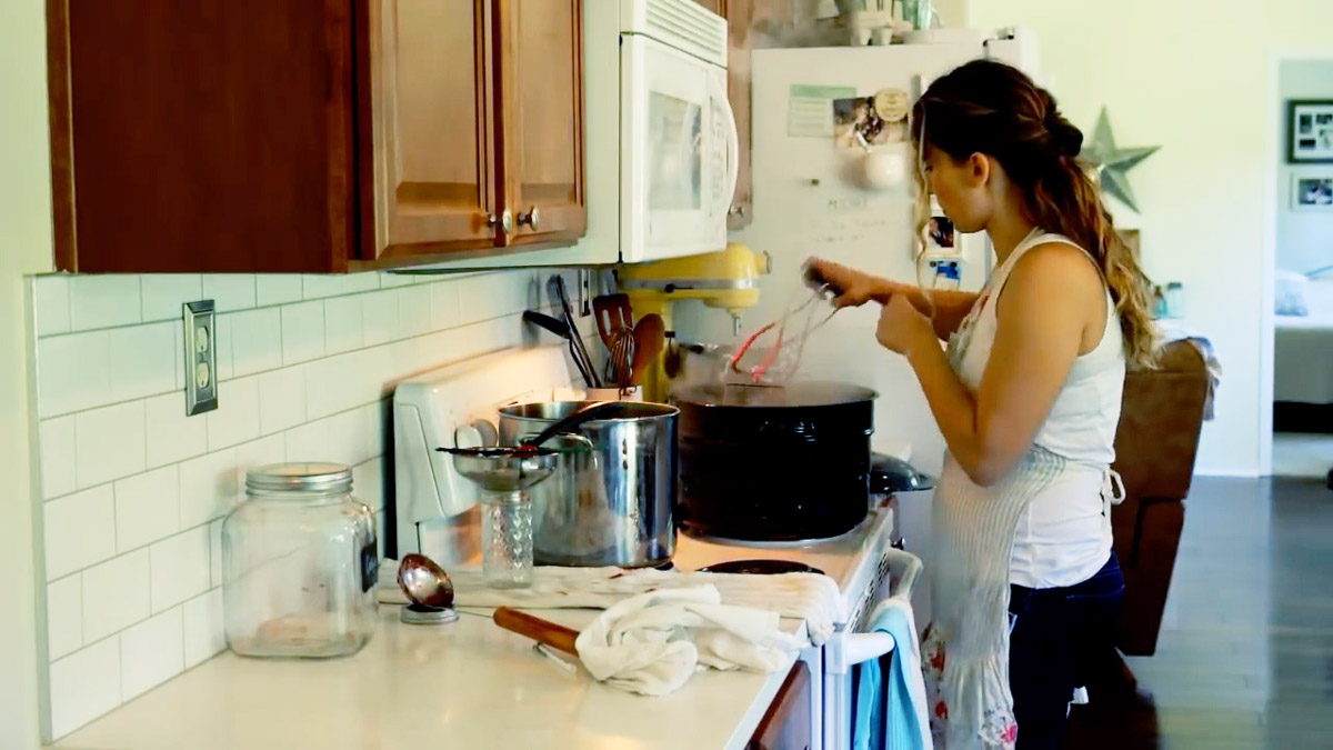 A woman placing jars full of strawberry jam into a water bath canner for processing.