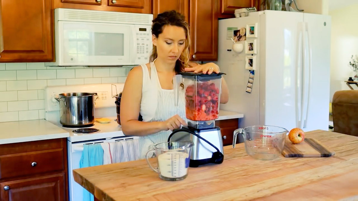 A woman blending strawberries in a blender.