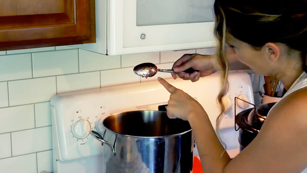 A woman lifting a chilled spoon dipped in strawberry jam to demonstrate sheeting.
