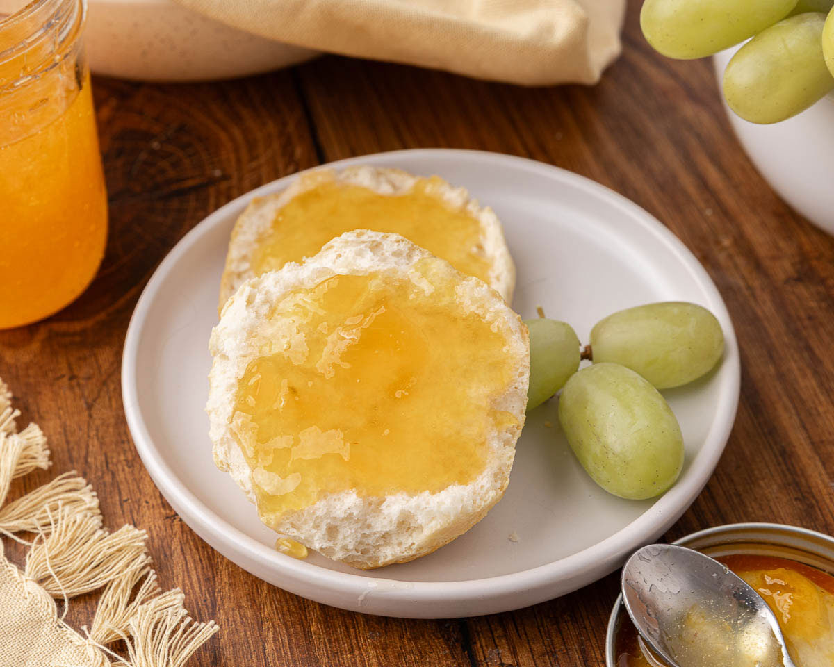 A biscuit topped with grape jelly, served on a white plate with green grapes.