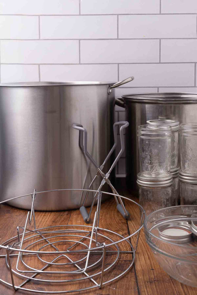 A stock pot, water bath canner. jar lifter, canning jars, lids, and steam rack.
