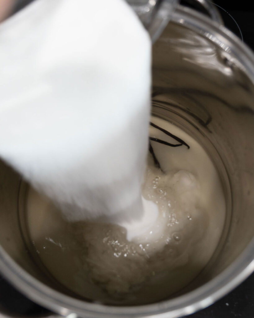 Pouring calcium water into a stockpot with grape juice to make jelly.