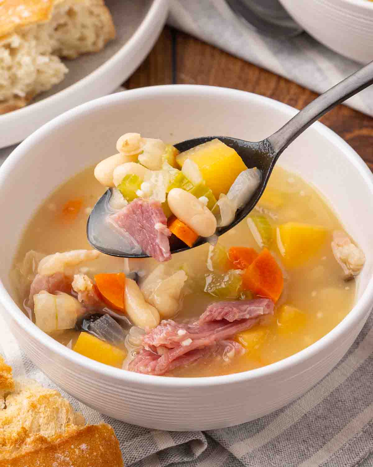 Ham and bean soup served in a white bowl with a spoon showing a bite for texture.