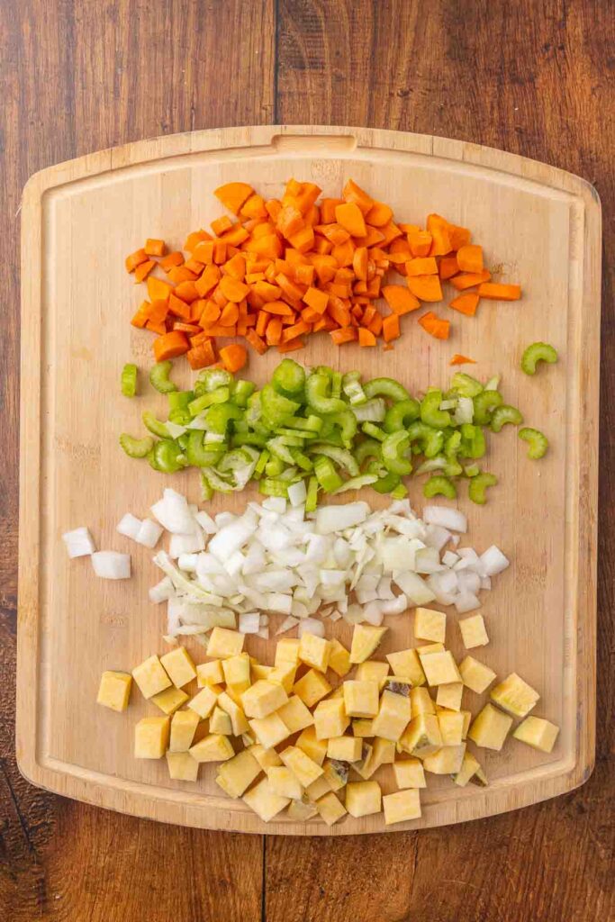Chopped carrot, celery, onion, and rutabaga on a wooden cutting board.