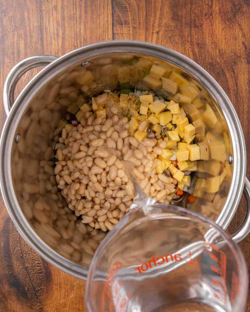 Adding water to a stock pot full of ham and bean soup ingredients.