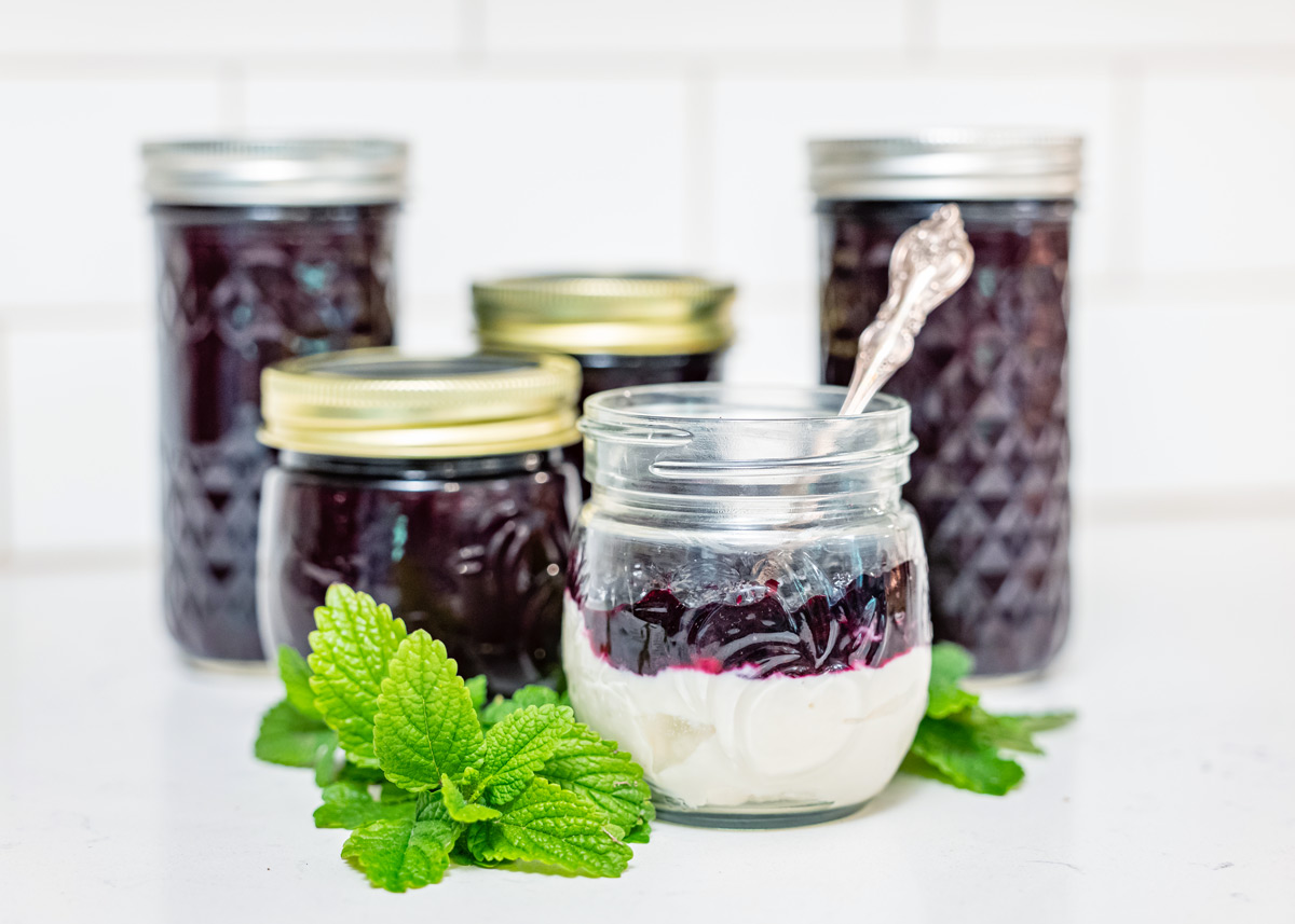 Jars of blueberry jam with a jar of yogurt topped with blueberry jam.