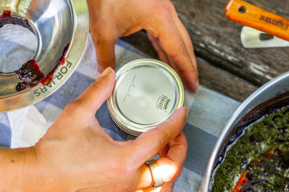 A woman tightening a canning lid onto a jar of blueberry jam.