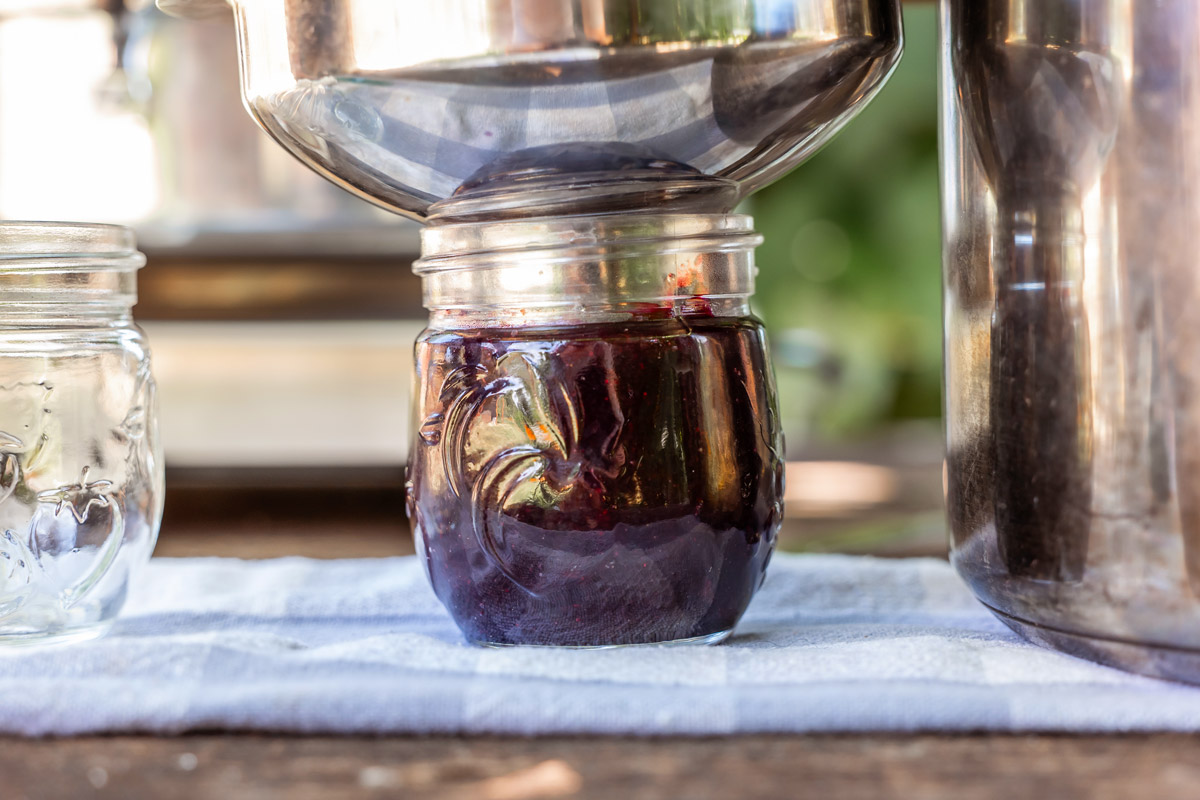 Blueberry jam being ladled into a jar.