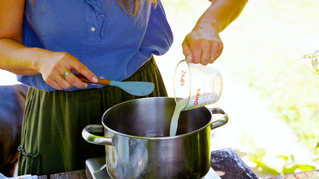 A woman adding lemon juice to a pot of blueberry jam.