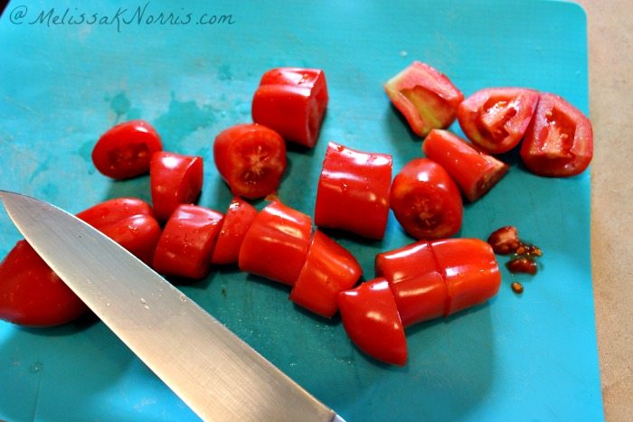 Sliced tomatoes on a blue cutting board with a knife.