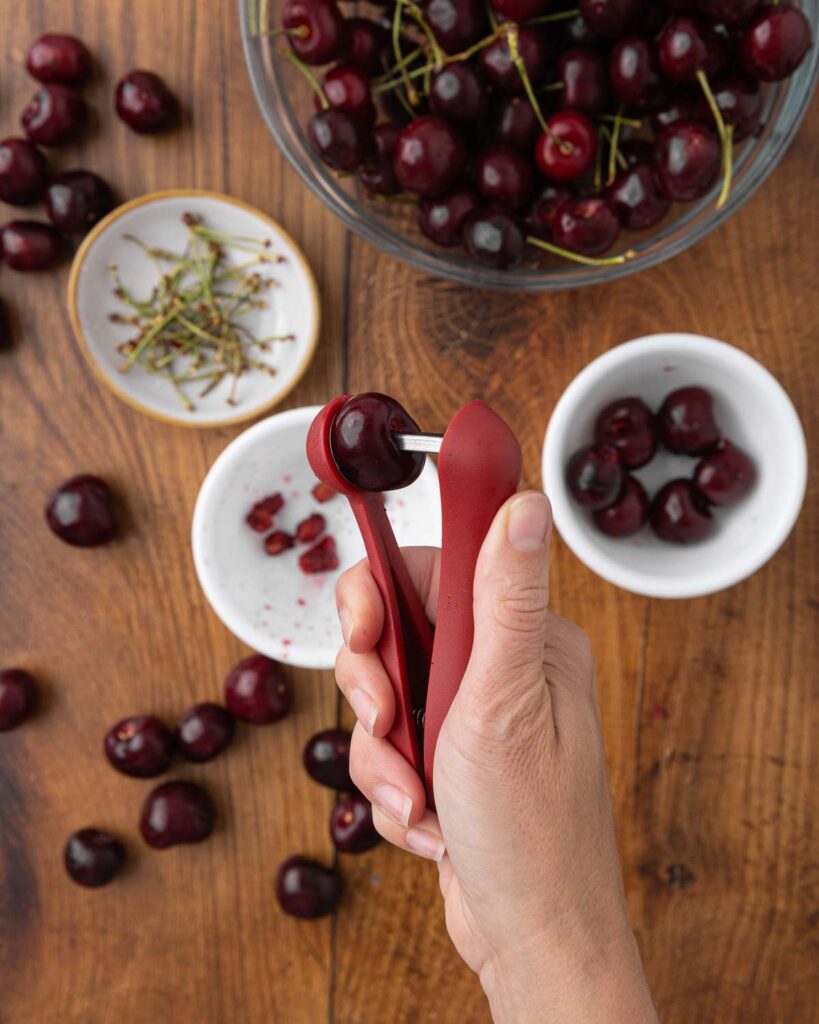 A hand pitting a cherry with a cherry pitter.