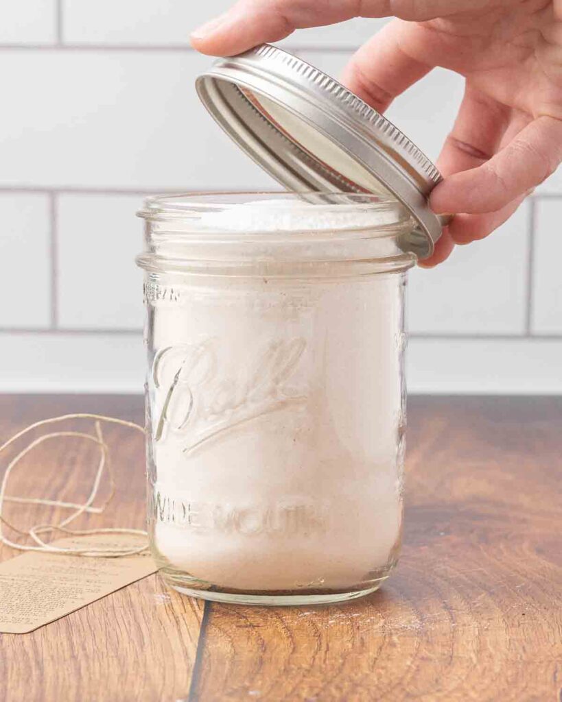 A hand placing a lid on a glass jar filled with biscuit mix.