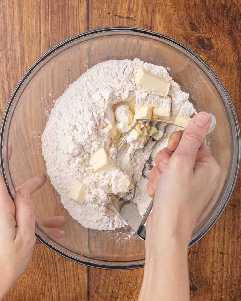 A hand using a pastry cutter to incorporate the butter into the dry biscuit ingredients.