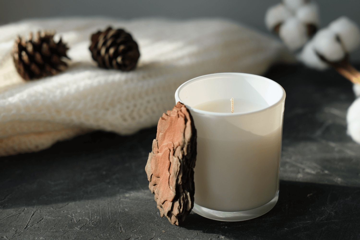 homemade soy candle in jar on table with blanket and pine cones