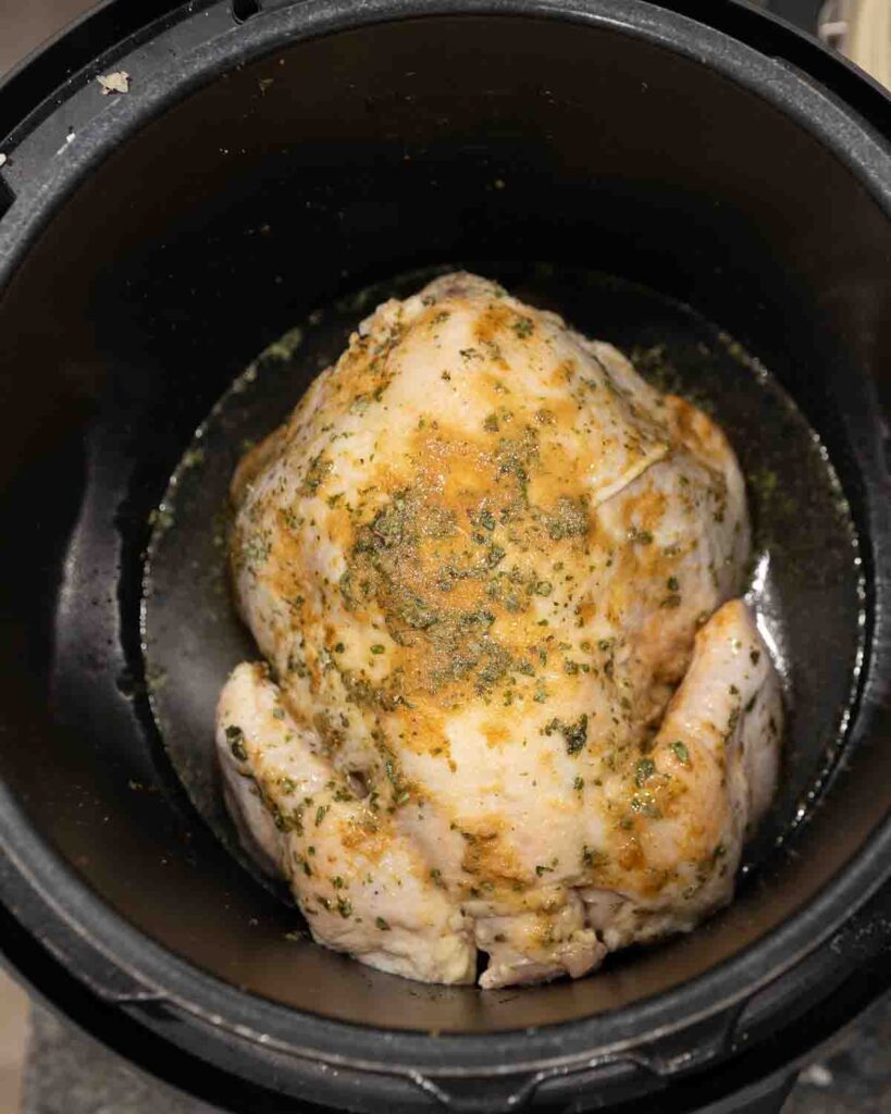 A seasoned raw whole chicken sitting inside an Instant Pot.