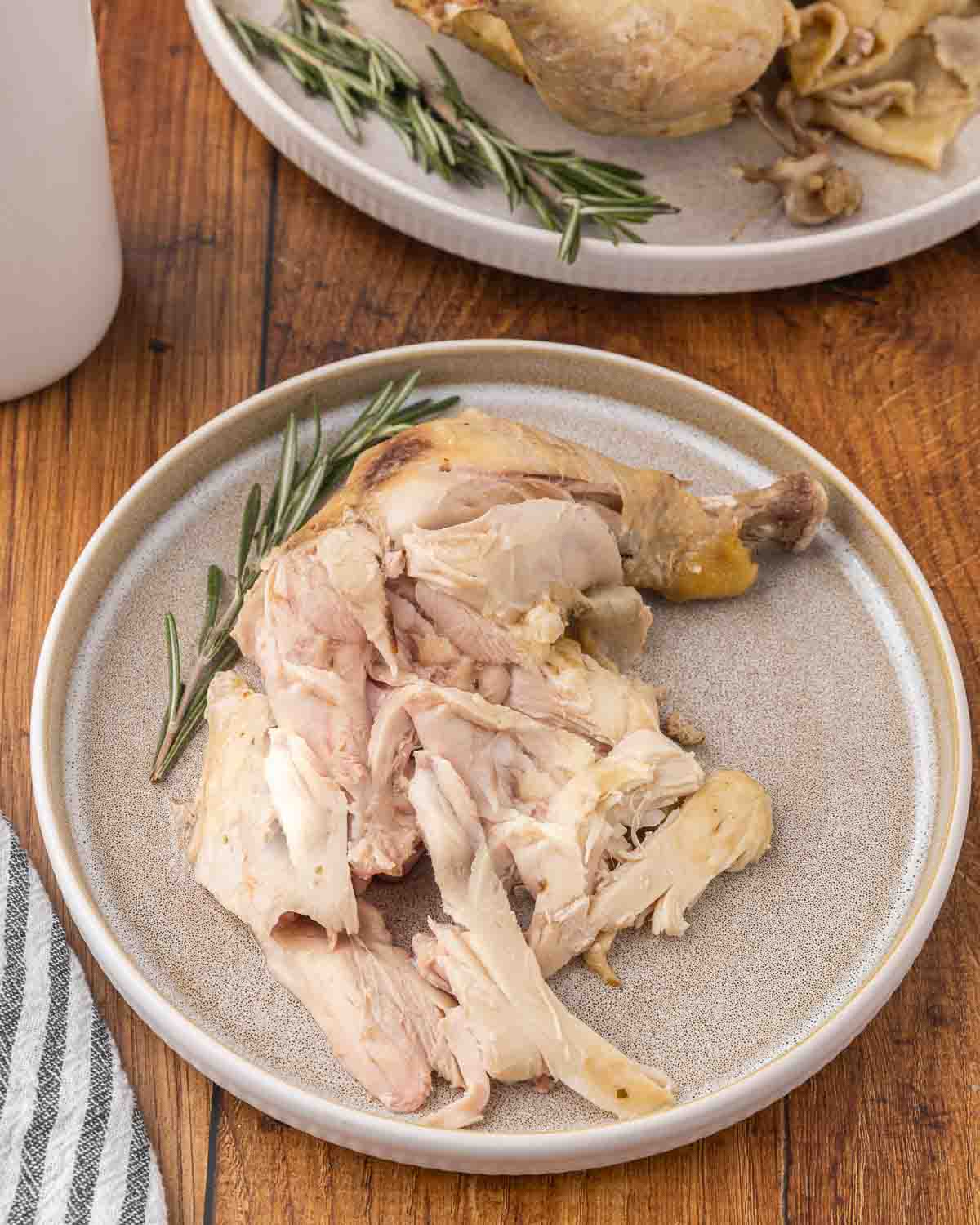 A cooked chicken thigh served on a white plate, and garnished with fresh rosemary.