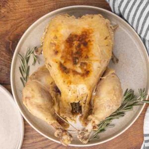 A cooked whole chicken served on a white platter and garnished with fresh rosemary.