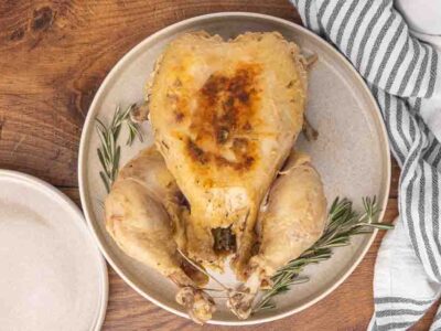 A cooked whole chicken served on a white platter and garnished with fresh rosemary.