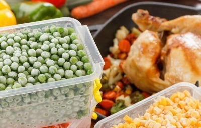 Frozen containers of peas and corn being added to a chicken dish.
