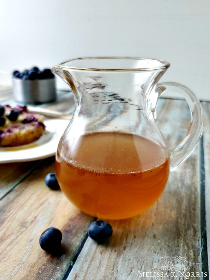 rosewater syrup in pitcher poured over blueberry pudding