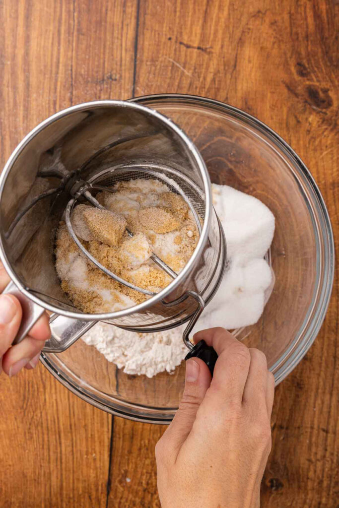 Hands using a sifter to blend dry ingredients for vinegar pie.