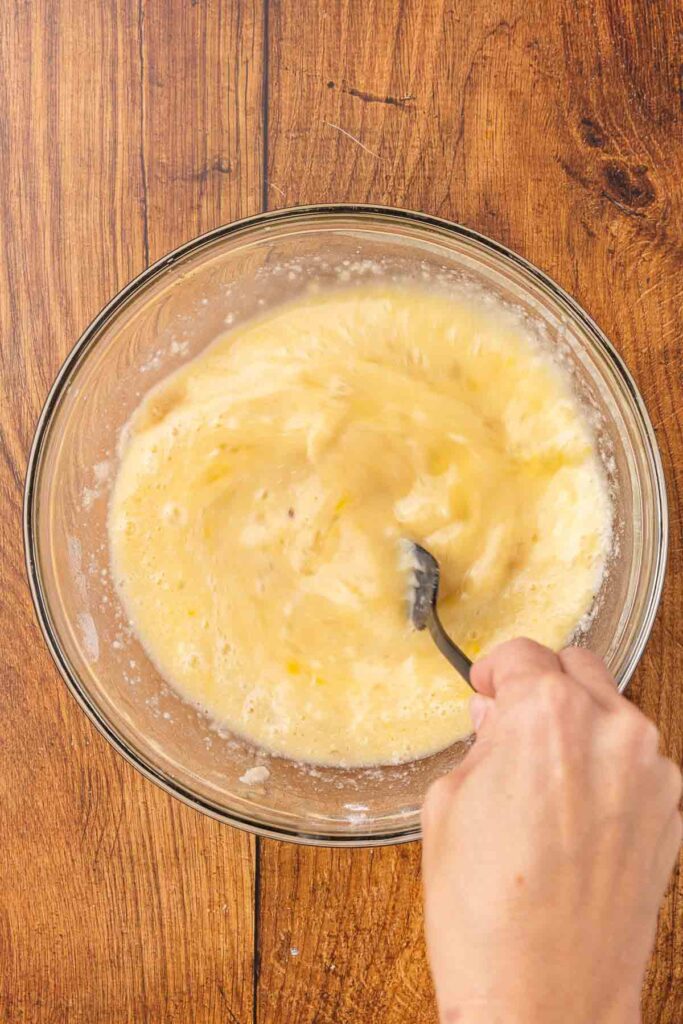 A hand using a spoon to mix wet and dry vinegar pie ingredients together in a bowl.