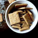 White bowl filled with homemade crackers sitting on a cookie sheet with more crackers.