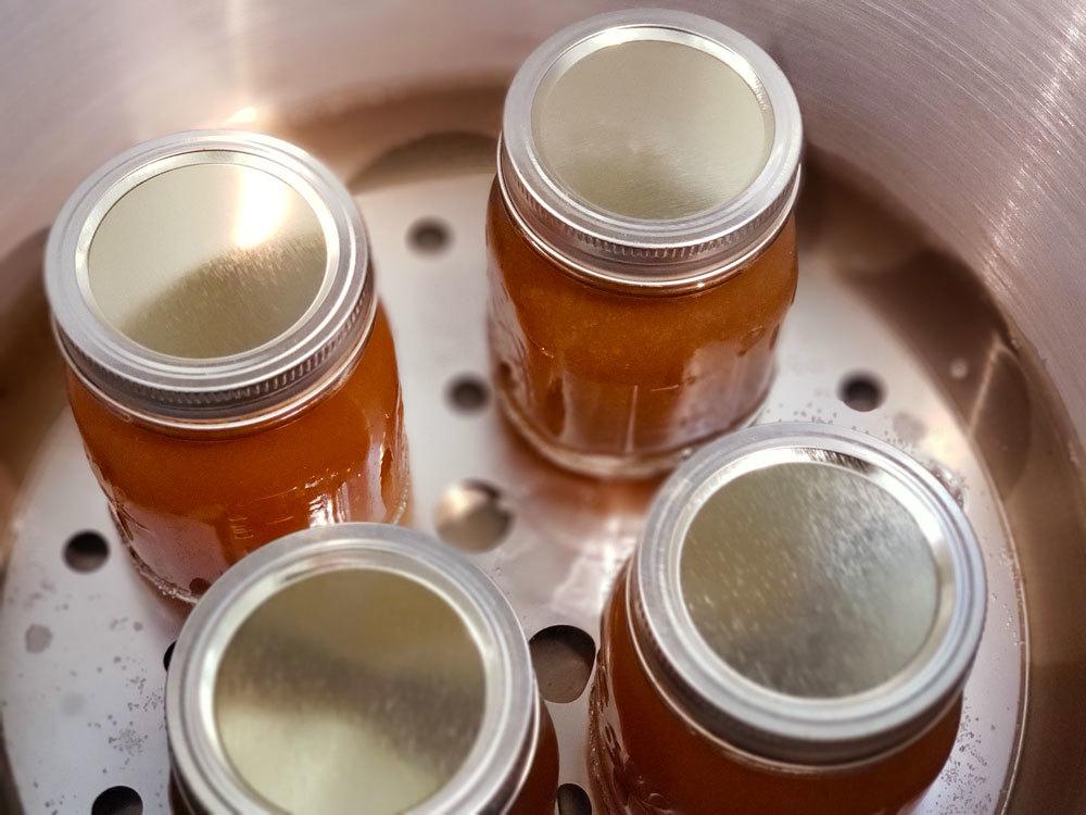 Mason jars being filled with chicken broth with a ladle and funnel.