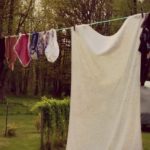 Image of clothes hanging from a clothesline with the sun setting in the background. Text overlay says, "5 Reasons to Use a Clothesline".