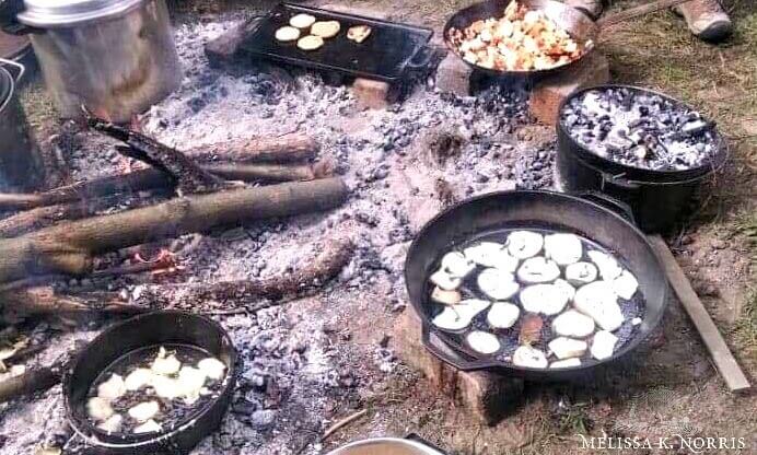 Cast iron pans over hot coals cooking food.