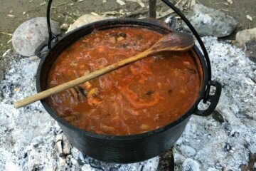 A dutch oven filled with soup, hanging over an open fire.