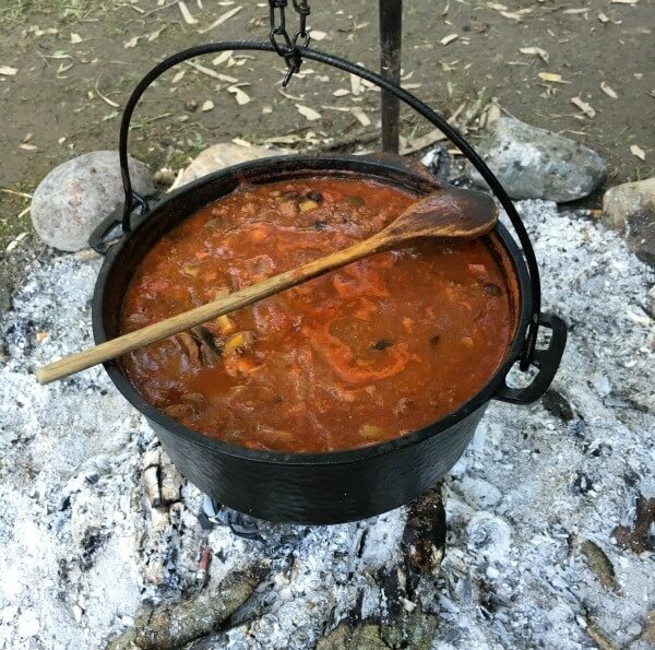 A dutch oven filled with soup, hanging over an open fire.
