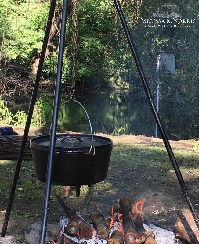 A dutch oven hanging from a tripod over an open fire.