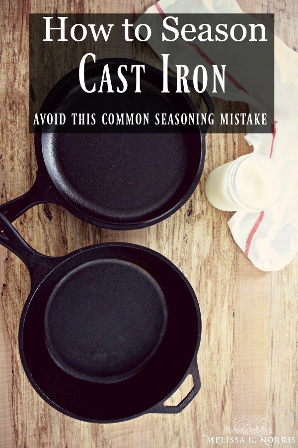 Two cast iron pans sitting on a wood table with a cloth and jar of lard. Text overlay says, "How to Season Cast Iron: Avoid this Common Seasoning Mistake".