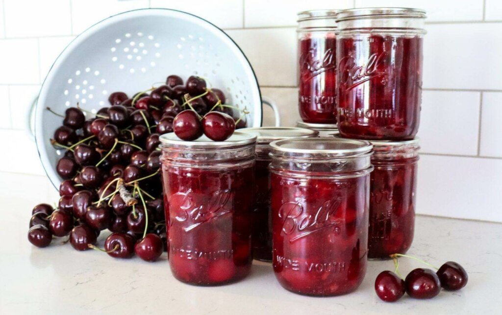 Jars of canned cherries and a spilled bowl of fresh cherries on the counter.