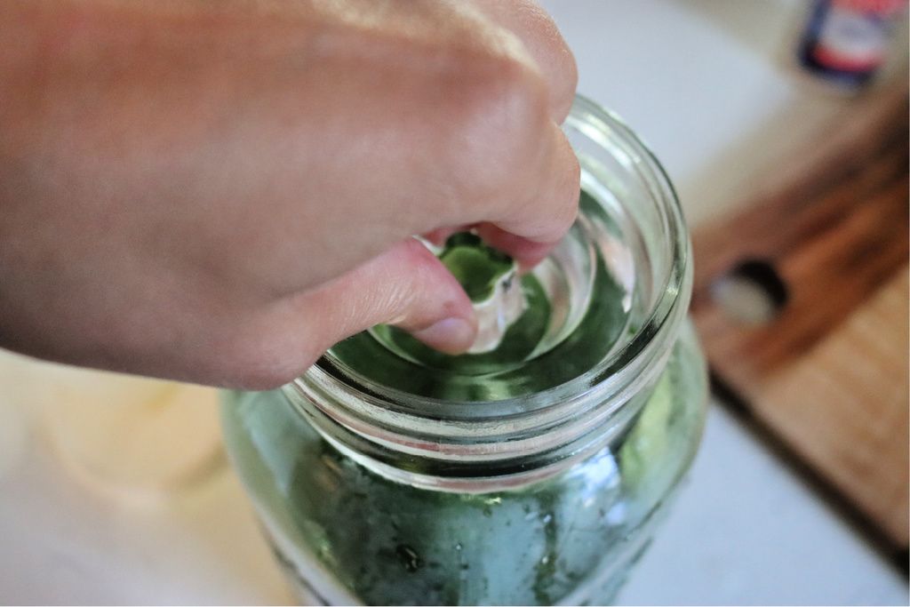 A hand placing a fermenting weight into a mason jar filled with pickles and brine.