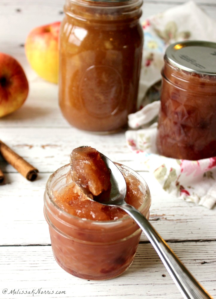 Three jars of apple pie jam on a white washed wooden table with cinnamon sticks and apples in the background. "Best Apple Pie Jam: Low sugar & my easy canning instructions"