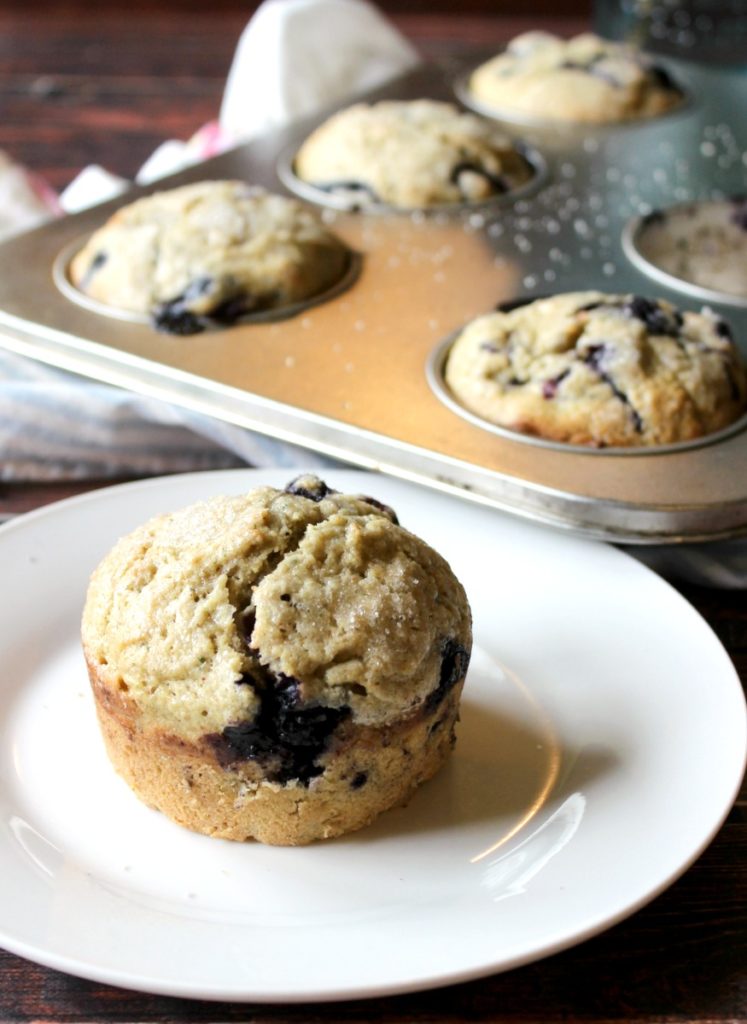Blueberry zucchini muffin on a white plate with a muffin tin in the background.