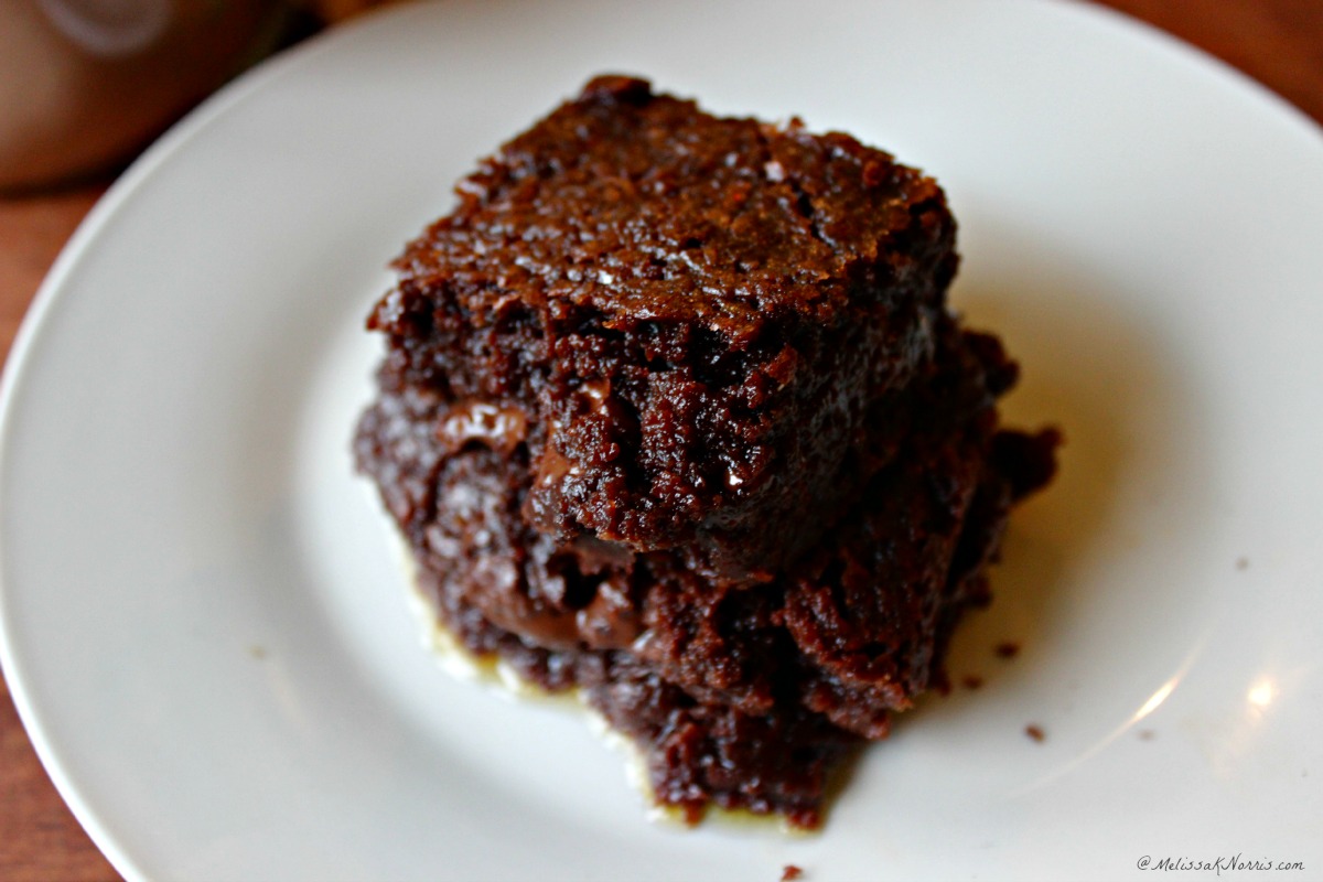 Picture of a white plate holding a a fudgy brownie. Sitting on the table in the background is a Mason jar filled with homemade brownie mix. Text overlay says "Homemade Brownie Mix in a Mason Jar".
