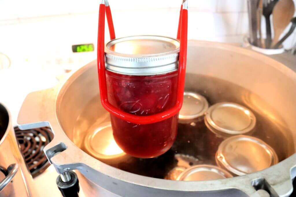 colander of cherries and jars of homemade cherry pie filling on white counter