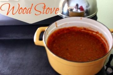 Image of a wood stove with a large stock pot of soup on top. Text overlay says, "How to Cook on a Wood Stove".