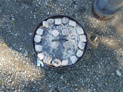 A dutch oven pan and lid covered in hot coals.