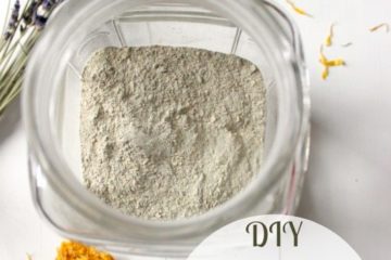 Image is a bird's eye view of an open jar filled with Bentonite clay. Scattered around it are sprigs of dried lavender and dandelion heads. Text overlay says, "DIY Herbal Bentonite Clay Face Mask and Scrub".