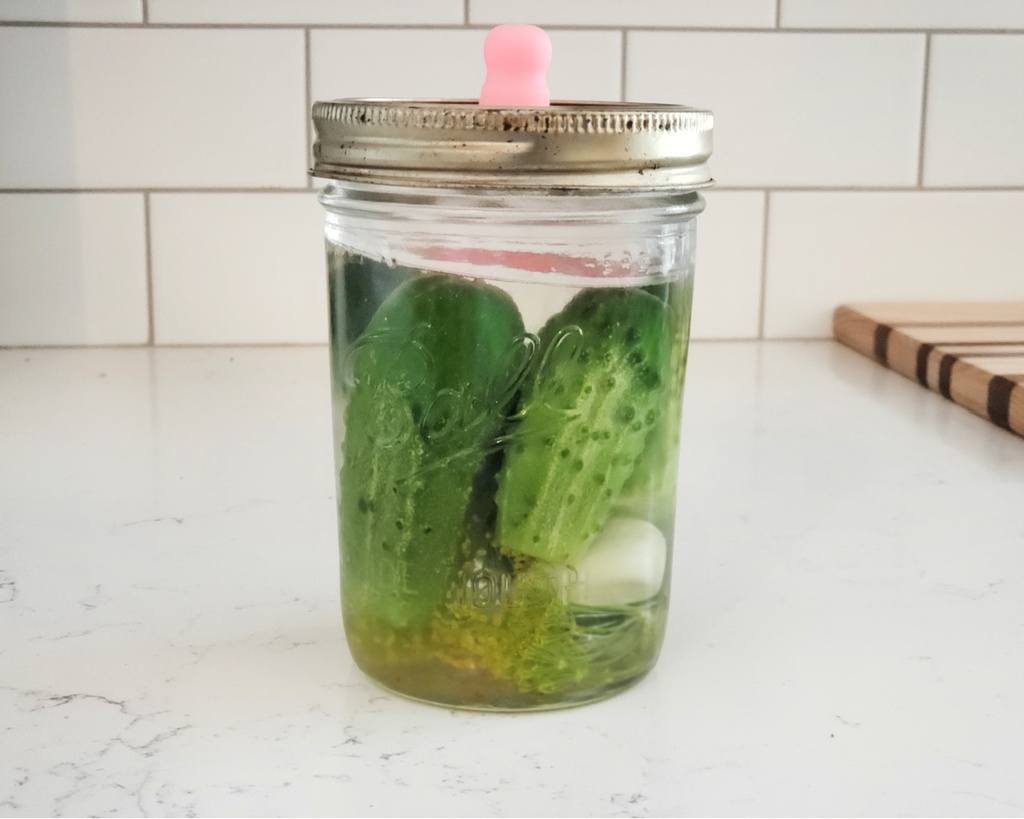 A jar of fermented pickles sitting on a counter.