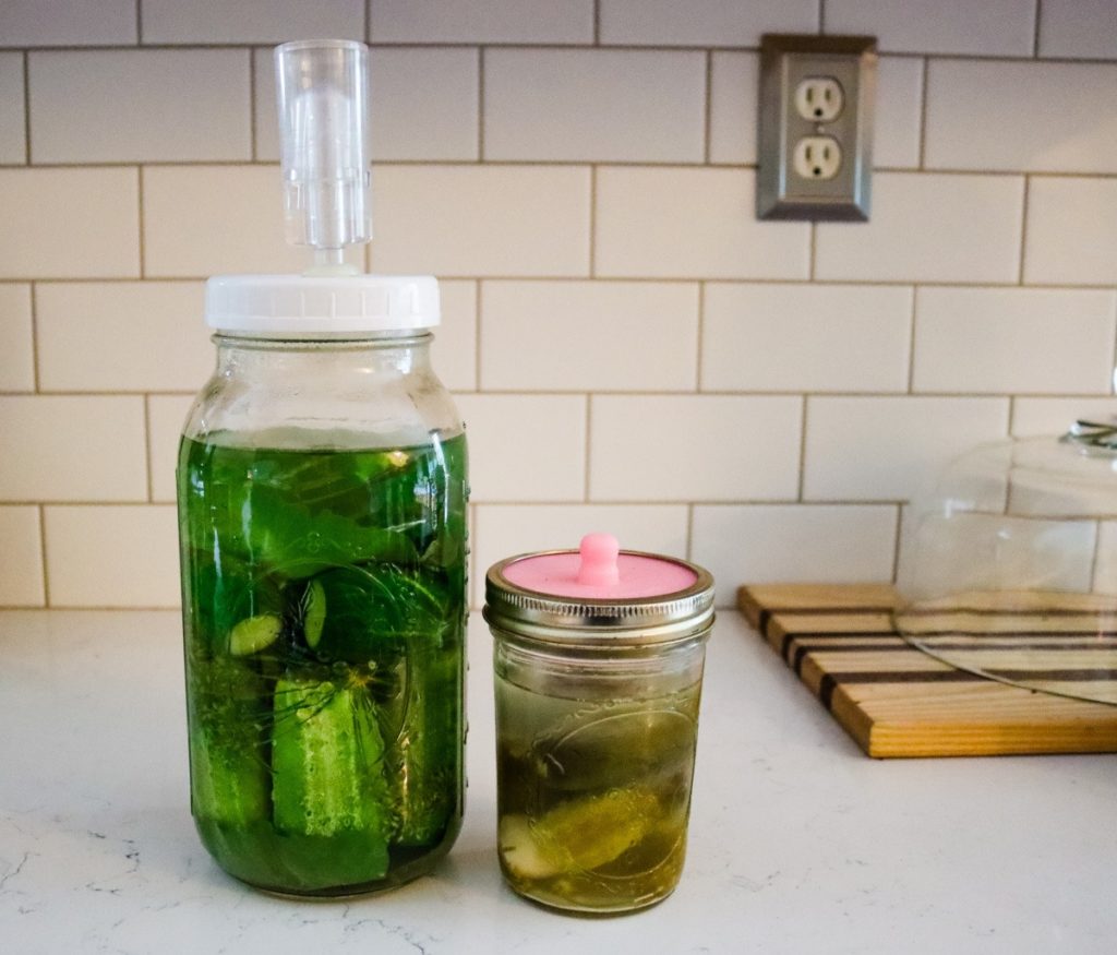 Mason jar filled with pickles sitting on a towel on a table. Text overlay says, "Old Fashioned Salt Water Brine Fermented Pickles."