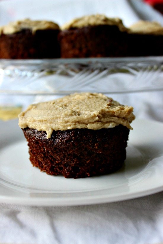 Close up image of a frosted chocolate cupcake on a white plate with a cake tray full of cupcakes in the background. Text overlay says, "Chocolate Mayo Cupcakes with Caramel Frosting".